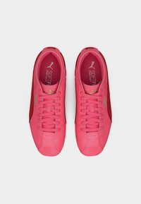 Ροζ σουέντ αθλητικά παπούτσια με απαλή υφή, διακοσμημένα με κόκκινο λεπτομέρειες, επίπεδα κορδόνια και ενσωματωμένο πάτο με χρυσά γράμματα.