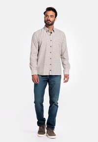 Lichtbeige geblokte blouse met lange mouwen, gecombineerd met blauwe jeans en grijze sneakers. De blouse heeft zwarte knopen en een kraag.