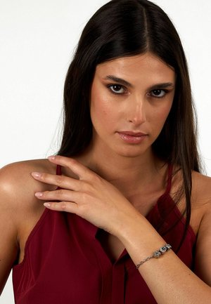 Bracciale d'argento con accenti testurizzati e dettaglio circolare, indossato su un polso nudo, che completi un top senza maniche di un rosso intenso.