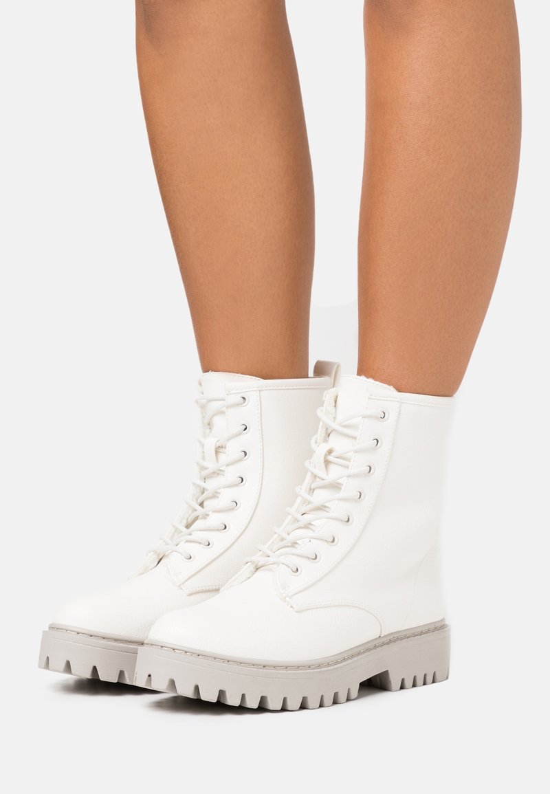 Valkoiset nauhakiinnitteiset nilkkasaappaat, joissa on teksturoitu nahkapinta, chunky harmaa ulkopohja ja pehmustettu kaulus.