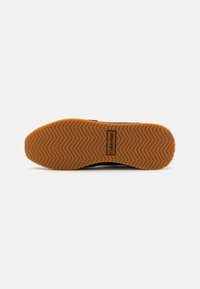 Black sneaker with a textured rubber sole featuring a herringbone pattern and a tan accent. Logo "Calvin Klein" embossed on the sole.