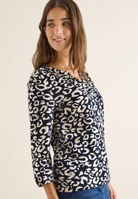 Blusa navy con stampa leopardata in crema. Presenta un scollo a V e maniche a tre quarti, con dettagli arricciati ai polsini. Tessuto morbido.