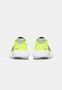 Neon gele sportschoenen met zwarte accenten en grijze veterogen, met een mesh bovenwerk en een gewatteerde witte zool voor comfort.