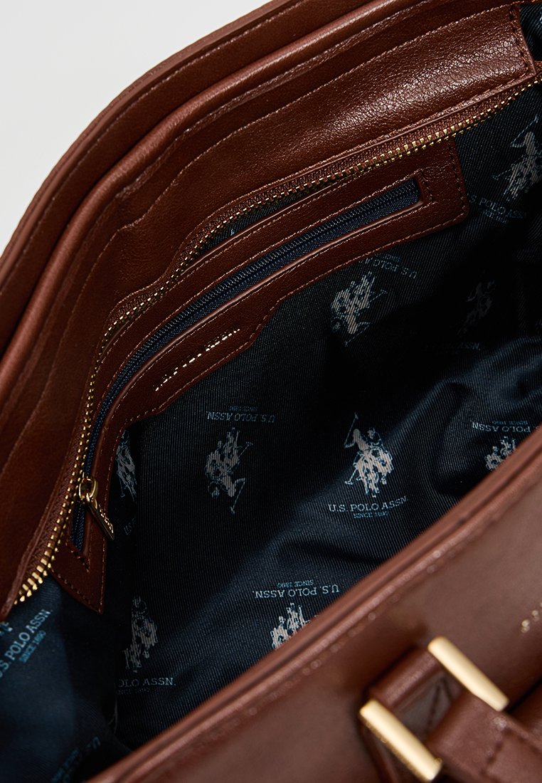 Intérieur d'un sac à main en cuir marron avec de multiples poches zippées, doublure en tissu foncé avec un motif de logo répété. Texture lisse, design spacieux.