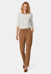 Haut léger blanc avec des manches trois-quarts, assorti à un pantalon beige à cordon de serrage et des chaussures à talons marron, présentant une coupe décontractée.
