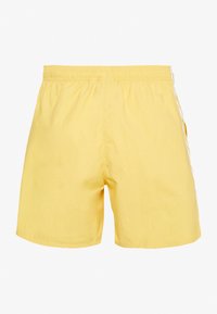 Yellow swim shorts made of lightweight fabric, featuring an elastic waistband and white side stripes on both legs. Classic, relaxed fit.