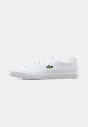 White sneaker made from synthetic material. Features a low-top design, lace-up closure, textured sole, and a green crocodile logo on the side.
