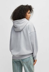 Grey oversized hoodie with a drawstring hood, ribbed cuffs and hem, and a soft texture. Worn with light blue denim jeans.
