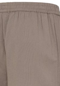 Detailný záber na béžové látkové nohavice s elastickým pásom a detailom bočného vrecka.