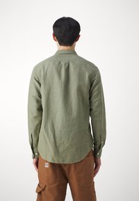 Camicia verde a maniche lunghe realizzata in un tessuto strukturiert con colletto a camicia. Presenta un orlo curvo e polsini con bottone.