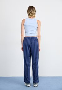 Haut sans manches bleu clair au design ajusté, associé à un pantalon rayé bleu marine en tissu doux avec une taille élastique, porté avec des baskets grises.