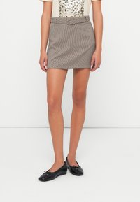 Mini gonna a scacchi grigi e neri con cintura, superficie liscia e design aderente, abbinata a ballerine nere.