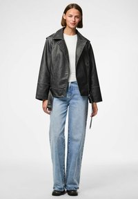 Veste de motard en simili cuir noir avec des revers larges et des coutures blanches contrastées ; associée à un jeans taille haute bleu clair. Chaussures noires.