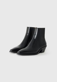 Bottines noires à bout pointu, finition brillante et petit talon empilé. Les côtés présentent des détails en côtes verticales.