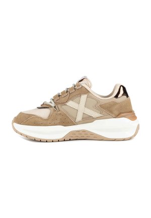 Zapatilla beige y marrón claro con suela blanca gruesa, paneles de ante y malla, patrón cruzado en el lateral y detalle metálico en el talón.