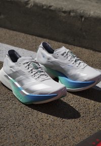 Een paar witte atletische hardloopschoenen met blauwe en groene gradientzolen geplaatst op asfalt vlak bij een stoeprand.