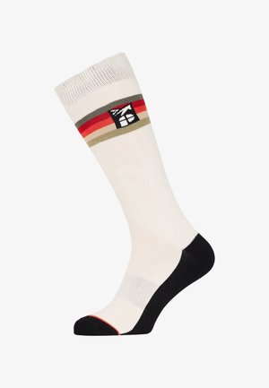 Knielange sok in crème met zwarte teen en hiel. Bevat horizontale strepen in rood en groen. Logo-patch nabij de bovenkant. Gladde textuur.
