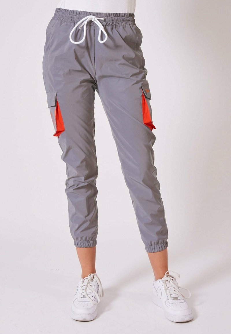 Pantalon de jogging gris avec cordon de serrage et rabats rouges à l'intérieur des poches, porté avec des baskets blanches, poignets élastiques aux chevilles visibles.