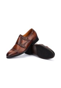 Bruine leren dubbele monkstrapschoenen met een strakke vormgeving, spitse neus en een getextureerde rubberen zool. Inclusief zilverkleurige gespen op de banden.