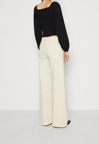 Top lungo a maniche smock nere con scollatura quadrata abbinato a pantaloni crema a vita alta e gamba larga. Entrambi i capi hanno una texture liscia.