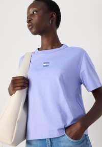Lavanda pamukasta majica s okruglim izrezom i kratkim rukavima. Ima mali logotip "Tommy Jeans" na prsima. Uparite s svijetloplavim trapericama.