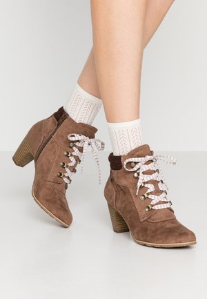 Brune ruskindsankelstøvler med stribede snørebånd, sidelås og blokhæle, båret med hvide mønstrede ankelstrømper på krydsede ben.