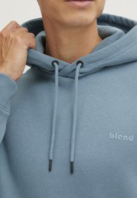 Felpa con cappuccio in cotone azzurro chiaro dal tocco morbido, con cordini regolabili e un piccolo logo sul petto.