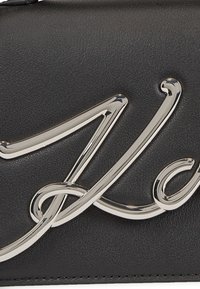 Clutch in pelle nera con dettaglio del logo in corsivo metallico argento. Texture liscia con linee pulite e design minimalista.