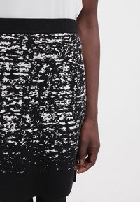 Jupe en tricot avec un motif abstrait noir et blanc. Elle présente une ceinture côtelée noire unie et une texture lisse.
