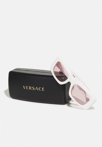 Valkoiset suurikokoiset aurinkolasit, joissa on vaaleanpunaiset linssit, yhdessä mustan Versace-laukun kanssa, jossa on kultakirjailuja.