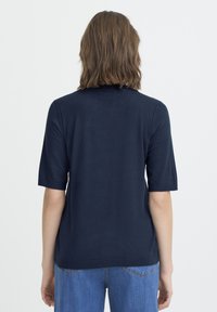 Tengerészkék rövid ujjú kötött felső kerek nyakkal, sima textúrával és bordázott szegéllyel az ujjvégeken és az alján. A hátulnézetnél minimális részletezés látható.