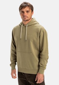 Olive green hoodie with front pocket, adjustable drawstring hood, and white accent laces. Soft texture, relaxed fit, minimal branding.