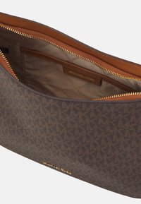 Cartera de tela marrón con monograma y cierre de cremallera, con un interior beige y una placa de logo dorada en el interior. Exterior texturizado y forro suave.