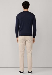 Maglione blu navy a maglia con maniche lunghe, abbinato a pantaloni beige chiaro. Design semplice con scollatura a girocollo e senza motivi o decorazioni visibili.