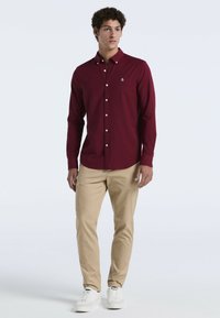 Bordeaux button-up shirt gemaakt van katoen, met een kraag en witte knopen. Gecombineerd met lichtbeige broek en witte sneakers.
