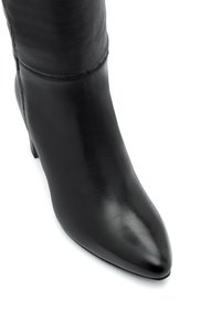 Czarny skórzany kozaki na wysokim obcasie z szpiczastym noskiem i widocznymi przeszyciami na cholewce, na białym tle.
