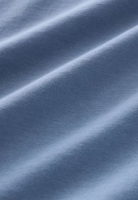 Hele sinine puuvillane kangas sileda tekstuuriga, millel on lainelised voldid, mis loovad õrna tooni ja läike variatsiooni.