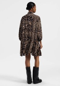 Abito con stampa leopardata, colletto alto, maniche lunghe e orlo arricciato, abbinato a stivali neri fino al ginocchio. Tessuto morbido e fluido, con un motivo testurizzato.