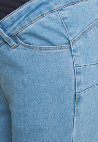 Ljusblå denimjeans med en figurnära design. Har detaljerad sömnad och en sidokasse. Tygets textur är slät med lätt stretch.