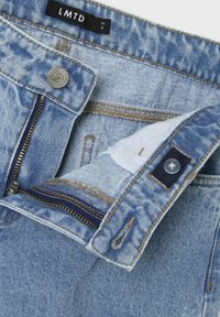 Ljusblå denimjeans med dragkedja, knapp av mässing och kontrasterande sömmar. Etiketten säger "LMTD." Funktionell design av bakfickor.