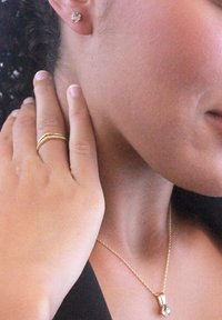 Set di gioielli in oro che include orecchini a bottone, una delicata collana con pendente e un anello avvolgente testurizzato, mostrati su una mano vicino al collo.