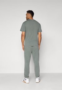 Γκρι βαμβακερό T-shirt και φόρμες, που δείχνουν χαλαρή εφαρμογή και απαλή υφή. Διαθέτει ελαστικές μανσέτες και κλασικά λευκά αθλητικά παπούτσια.