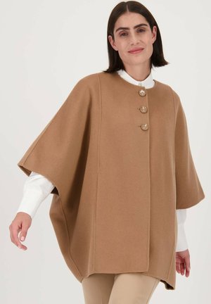 Bruine wollen cape met een ronde hals, vier knopen aan de voorkant en korte mouwen. Zachte textuur met een losse, relaxte pasvorm.