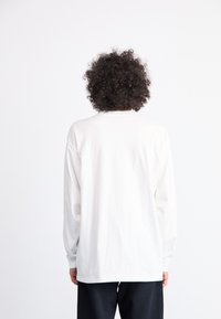Long-sleeve white cotton shirt with a rounded neckline and relaxed fit, viewed from the back, with slight stitching detail at the hem.