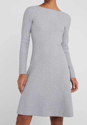 Frau trägt ein hellgraues, langärmliges, geripptes Strickkleid mit einem Bootsausschnitt, das in der Taille anliegt und im Rockteil leicht ausgestellt ist.