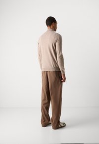Beige sweater with a round neckline and long sleeves paired with brown wide-leg trousers. Shoes feature green and white stripes.
