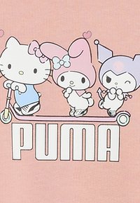 Różowa koszulka z grafiką, przedstawiająca postacie z kreskówek na skuterze. Postacie to Hello Kitty, My Melody i Keroppi. Logo "PUMA" w grubym białym kolorze.