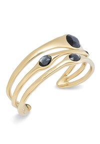 Bracelet à manche en tonalité dorée avec un design ondulé, mettant en avant quatre pierres noires facettées incrustées sur la surface. Texture lisse et polie.