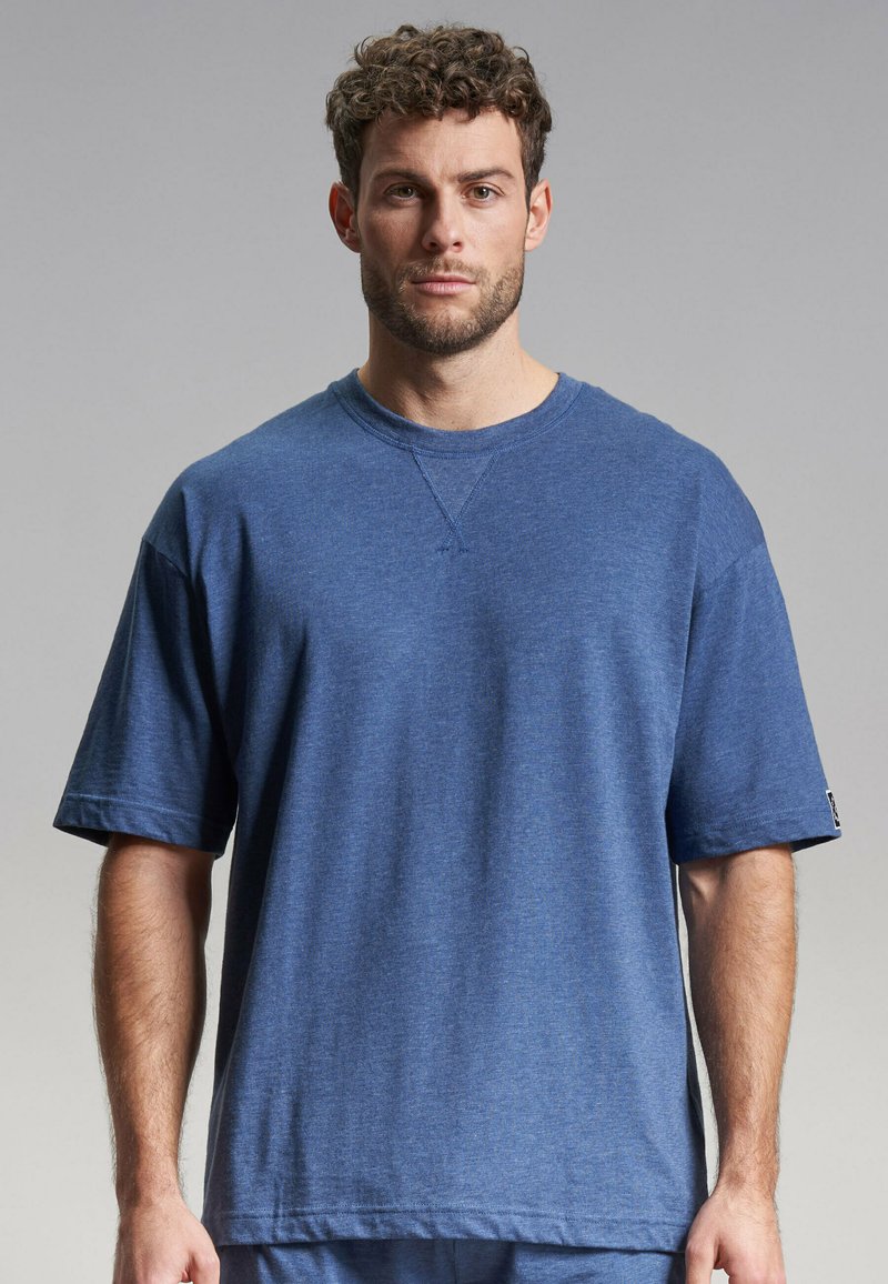 Camiseta de manga corta azul con cuello redondo, hecha de tela suave. Presenta un ajuste ligeramente holgado y detalles de costura mínimos en el escote.