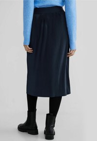 Black pleated midi skirt, made from a lightweight material, with a smooth waistband and a flowy silhouette. Paired with black ankle boots.